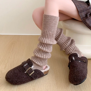 Gros plan de jambières en tricot beige portées avec des sabots en feutre marron