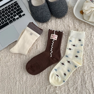 Three pairs of floral and striped mid-calf cotton socks on a soft plush carpet