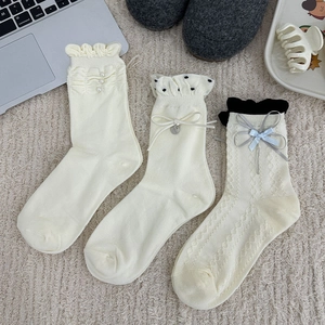 Trois paires de chaussettes mi-mollet beige avec perles, dentelle et nœuds sur un tapis