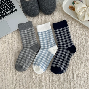 Three pairs of plaid cotton crew socks in blue and grey plaid patterns on a soft rug