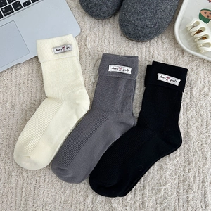 Close-up of three pairs of rib-knit mid-calf socks in white, grey, and black with fabric labels