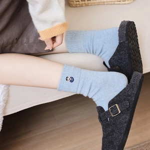 Close-up of light blue knitted socks with embroidery and grey felt buckled clogs