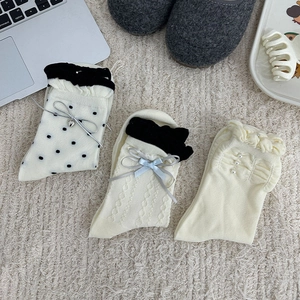 Détail de chaussettes mi-mollet blanc cassé avec perles, nœuds bleus et pois noirs