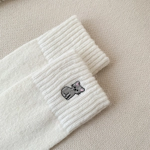 Close-up of cute grey cat embroidery on cream white ribbed wool knit socks