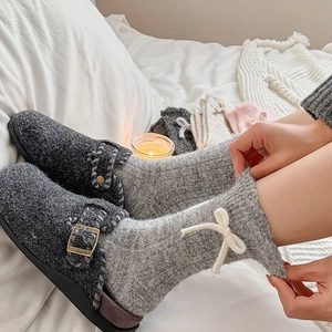 Detail of grey wool socks with white bows and plush slippers in a cozy home setting