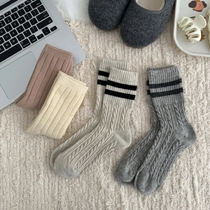 Close-up of four colors of cable-knit wool socks on a cozy plush rug with home decor