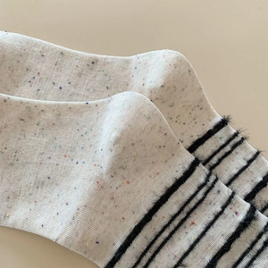 Detaillierte Nahaufnahme weißer Stricksocken mit bunten Sprenkeln und schwarzen Flauschstreifen
