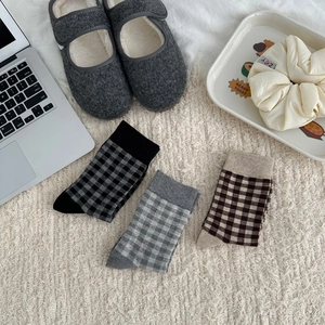 Flat lay of three pairs of plaid mid-calf socks in black, grey, and brown patterns