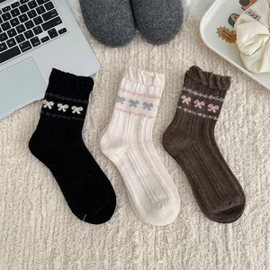 Macro detail of knit wool socks with bow patterns on a cozy white plush rug