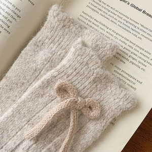 Detail of warm beige knit socks featuring a sweet ribbon bow and vertical ribbed texture