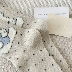 Detailed close-up of beige knitted socks with cute cartoon bears and black polka dots