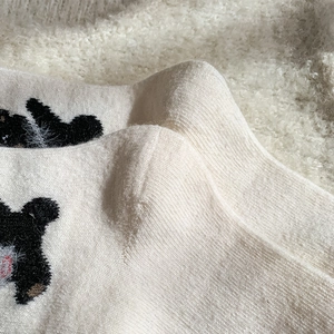 Detailed macro shot of soft cream wool socks with cute black bear embroidery pattern