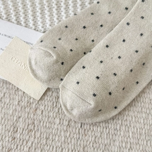 Close-up of beige knitted socks with black polka dots featuring reinforced toe detail