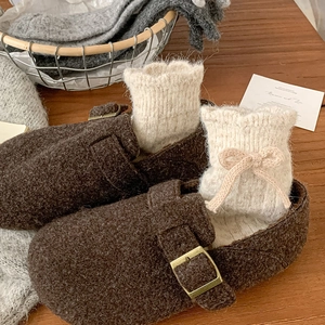 Close-up of ribbed knit socks with bow tie detail and brown wool mules on wood