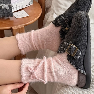 Detail of pink wool socks with knit bow and gray felt mules for winter warmth
