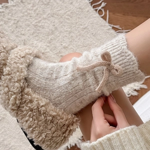 Cream knit leg warmers with ribbon bow paired with plush slippers for cozy winter style