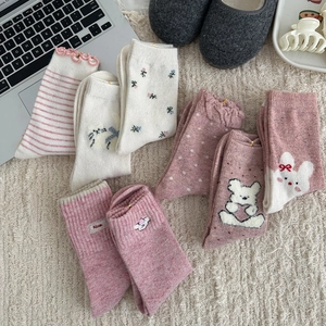 Pink and white wool socks with floral patterns and embroidery on a cozy rug