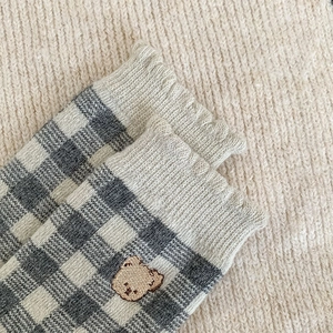 Close-up of grey plaid knit socks featuring cute bear embroidery and ribbed cuff texture