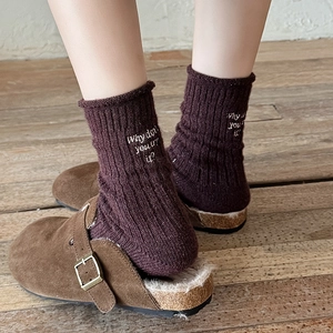 Detail of wool socks with white letter embroidery paired with brown fuzzy suede clogs