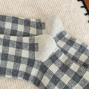 Close-up of gray and white checkered knit socks with cotton texture on beige blanket