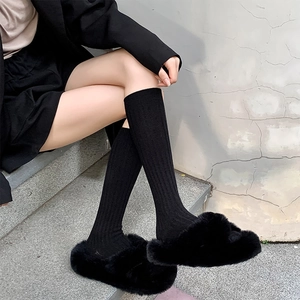 Close-up of black ribbed knit calf socks paired with black plush faux fur slippers