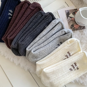 Close-up of thick wool socks with letter embroidery and rib knit texture on plush background