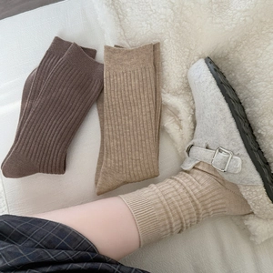 Detailed texture of thick ribbed knit socks in coffee tones on soft white plush rug