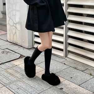 Detail shot of plush black slides styled with ribbed mid-calf socks on a city street