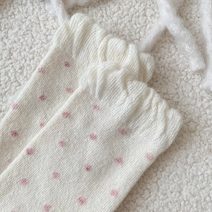 Close-up of white knitted wool socks with red polka dots and decorative ruffled edge trim
