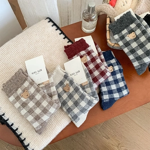 Detail view of five pairs of thick plaid socks with bear embroidery in warm autumn tones