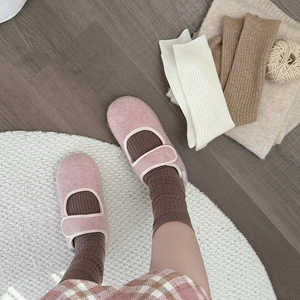 Pink Mary Jane plush slippers with brown ribbed socks on a white rug on wooden floor