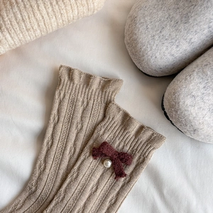 Detail of wool knit sock with a brown bow and white pearl accent in cozy setting
