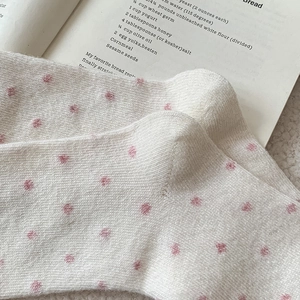 Detailed close-up of white knitted wool socks with pink polka dots on recipe book