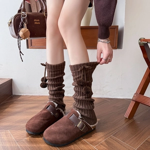 Detail of dark brown knit leg warmers with pompoms and suede faux fur clogs