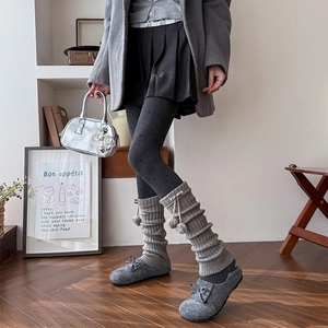 Detail of grey knitted leg warmers with fur balls and bows for cozy autumn style