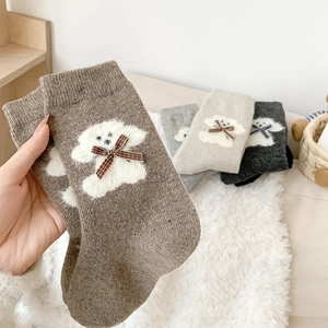Detail of wool socks featuring plush puppy motifs and checkered bows in warm autumn tones