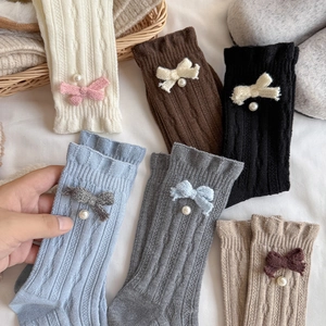 Detail of wool socks featuring knitted bows, pearl accents and wavy ruffled cuffs