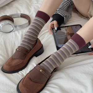 Brown suede loafers paired with purple and khaki striped knit socks on a cozy white bed