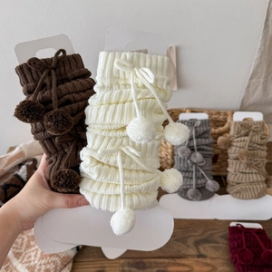 Close-up of cable knit leg warmers with bows and fluffy pom-poms in various colors