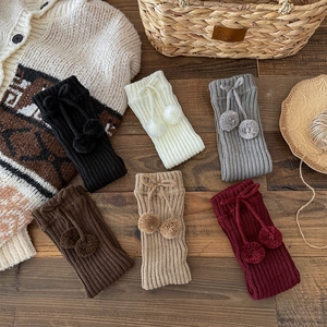 Detailed view of knitted leg warmers with ribbon bows and pompoms on vintage wood