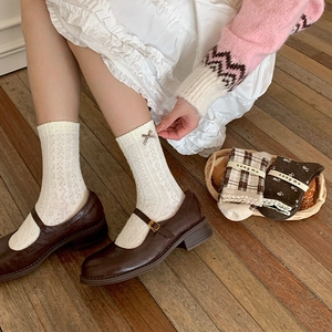 Detail of white pointelle knit sock with small bow accent and brown Mary Jane shoes