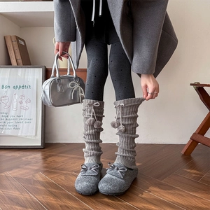 Close-up of grey ribbed knit leg warmers featuring sweet bow and plush pom-poms