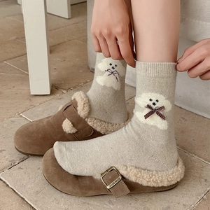 Oatmeal knit socks with plush dog motif and red bow paired with fuzzy brown slippers