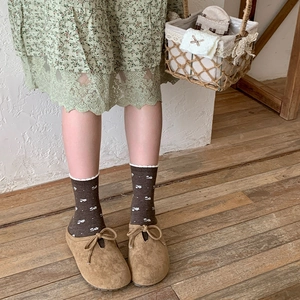 Detail of khaki suede clogs with bow and vintage floral socks on wooden floor