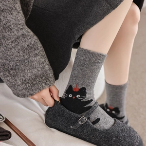 Detail shot of grey wool socks with cute black cat pattern wearing a red beret