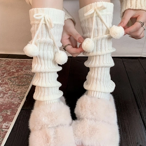Close-up of knit leg warmers with sweet bow ribbons and plush pom-poms on a soft cream base