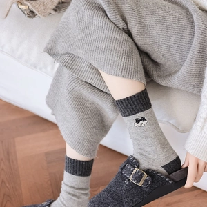 Close-up of thick knitted grey wool socks with cute white cloud embroidery and dark accents