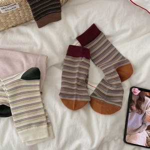 Flat lay of vintage striped cotton socks in warm color tones on soft white bedding
