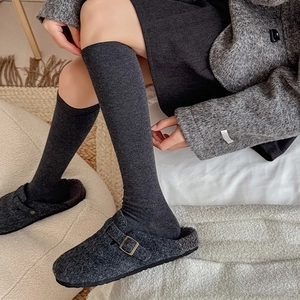 Close-up of thick dark grey over-the-knee socks paired with vintage buckle slippers