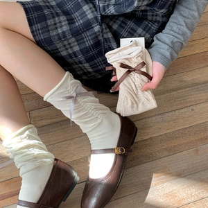 Detail of cream-colored slouch socks with silk ribbon bows and knitted rib texture